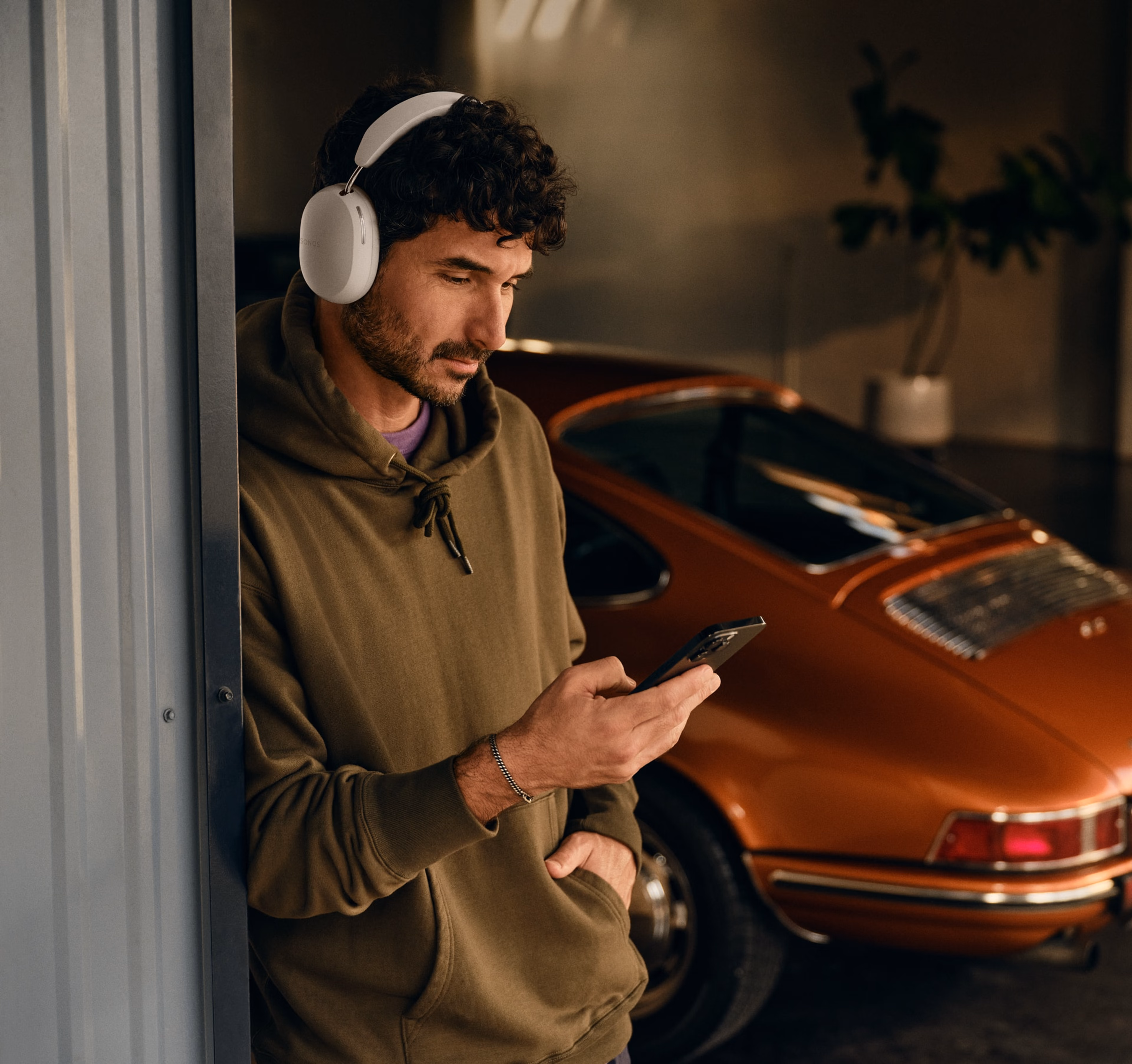 Person wearing white Sonos Ace and using his phone next to a car