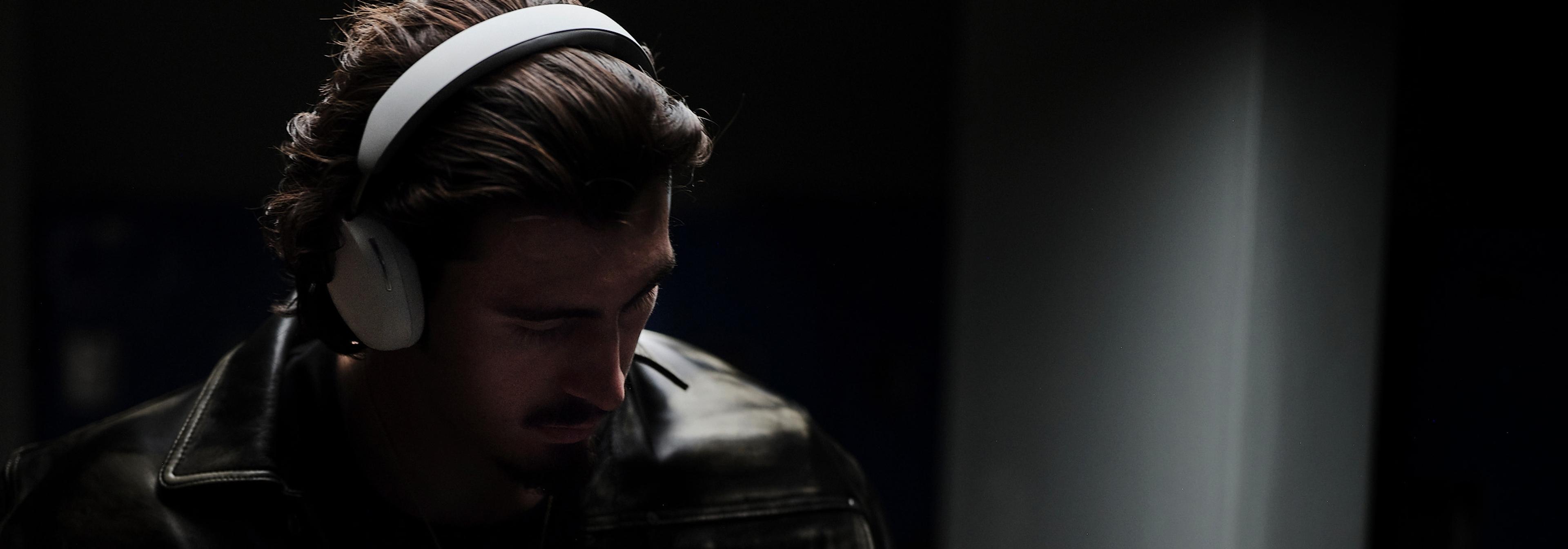 Person wearing a pair of white Sonos Ace headphones with dark black background