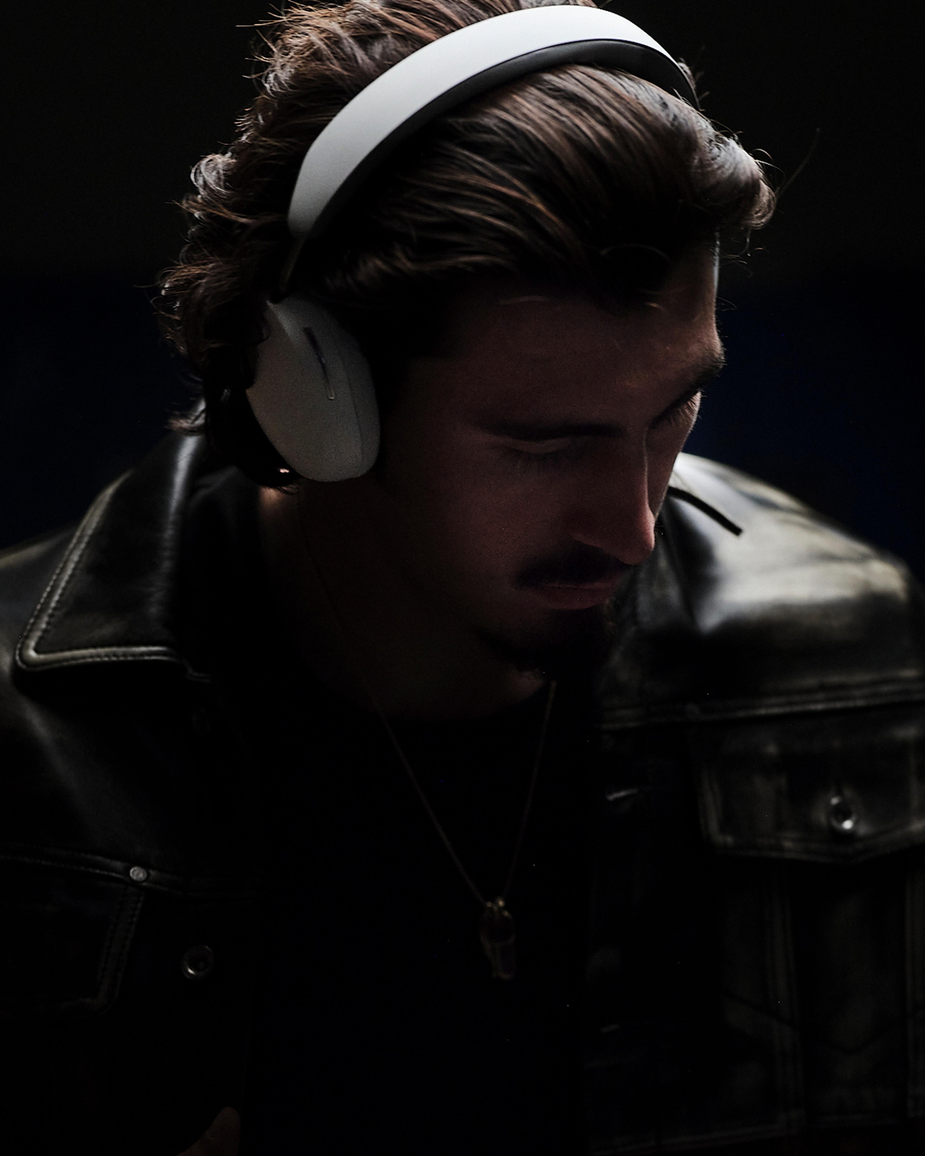 Person wearing a pair of white Sonos Ace headphones with dark black background
