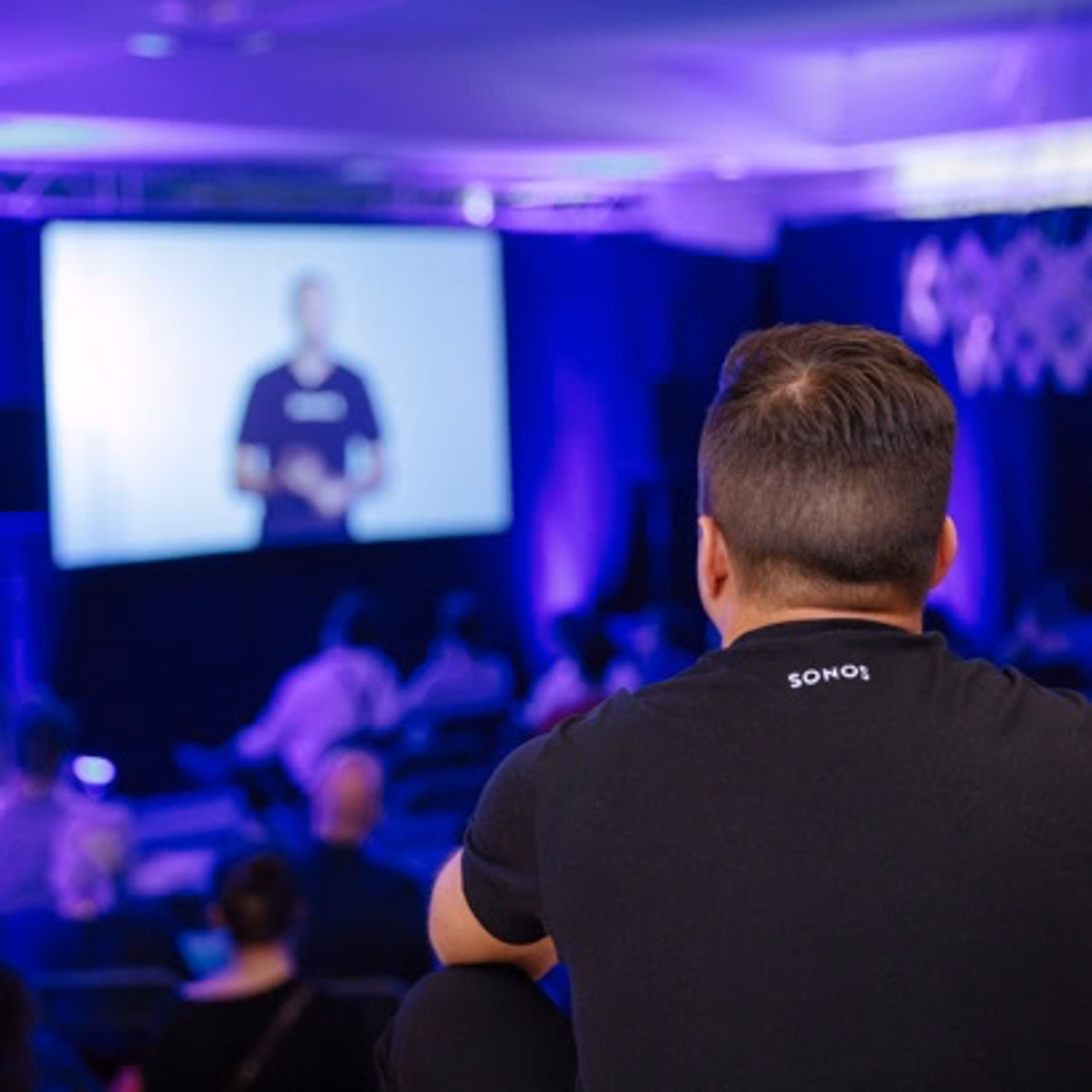 The back of a person's head at a conference listening and watching a video