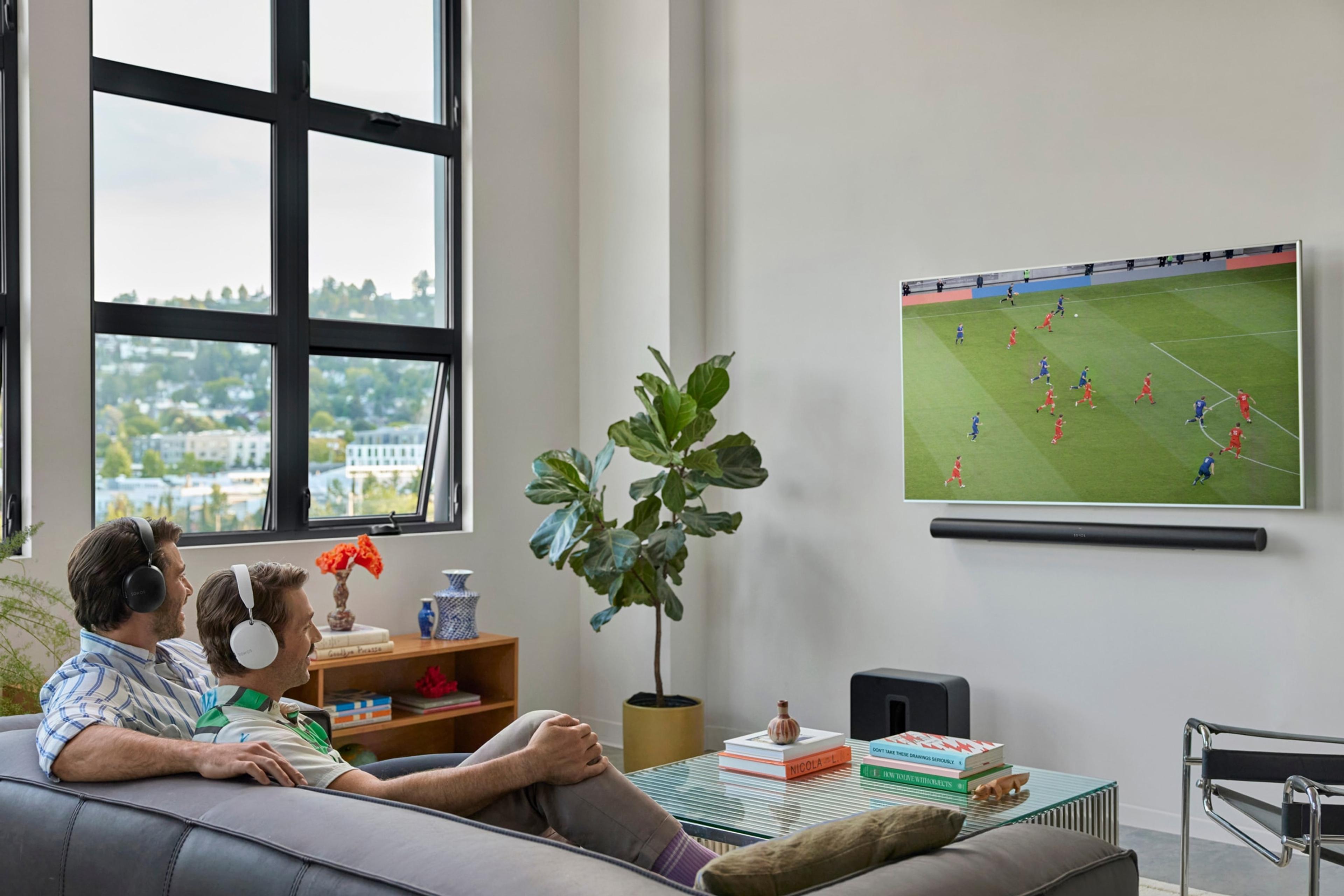 A couple on the couch watching a soccer match using audio swap from their Arc Ultra to their Sonos Ace headphones