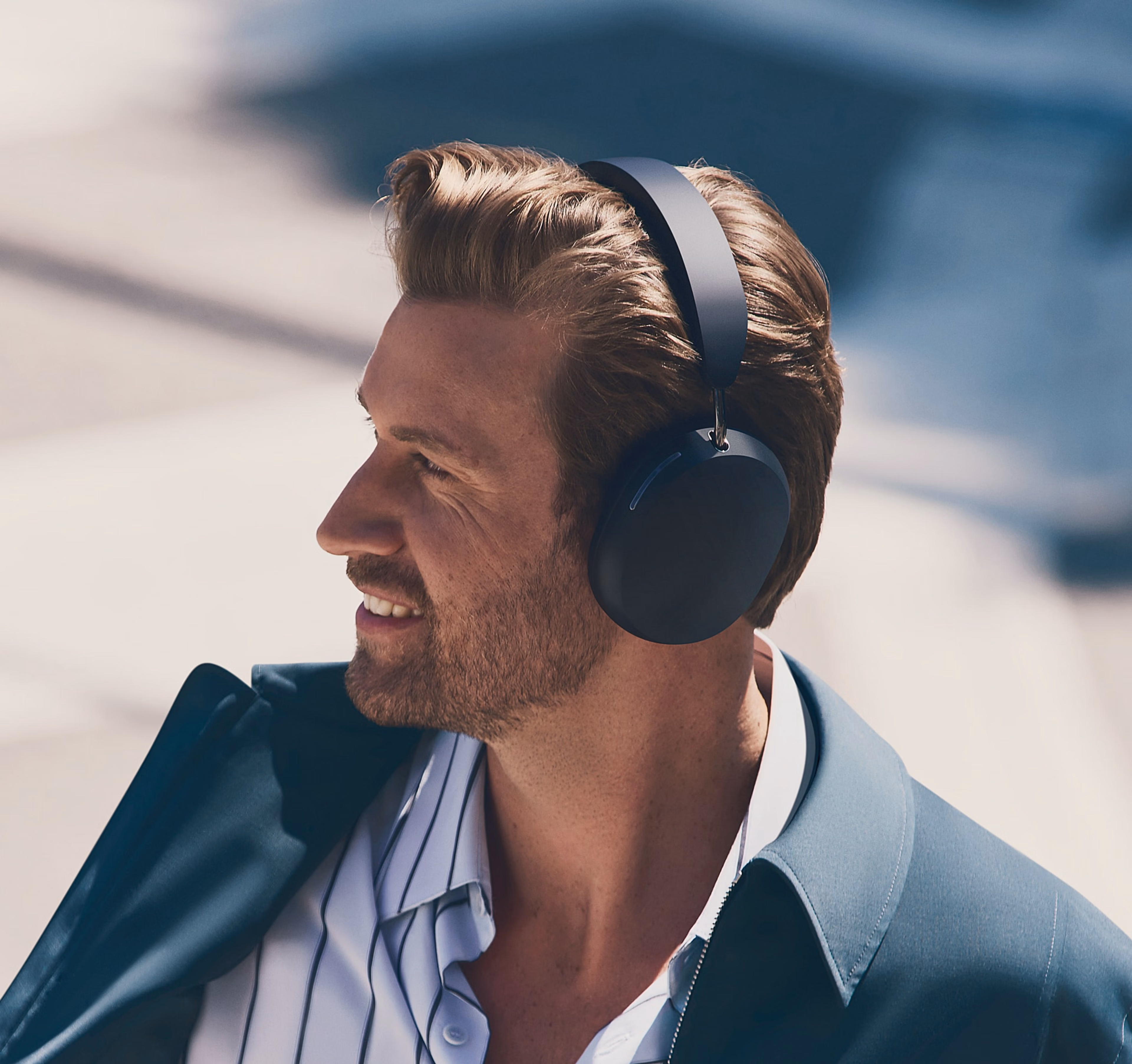 Person dressed in a suit wearing black Sonos Ace headphones outside