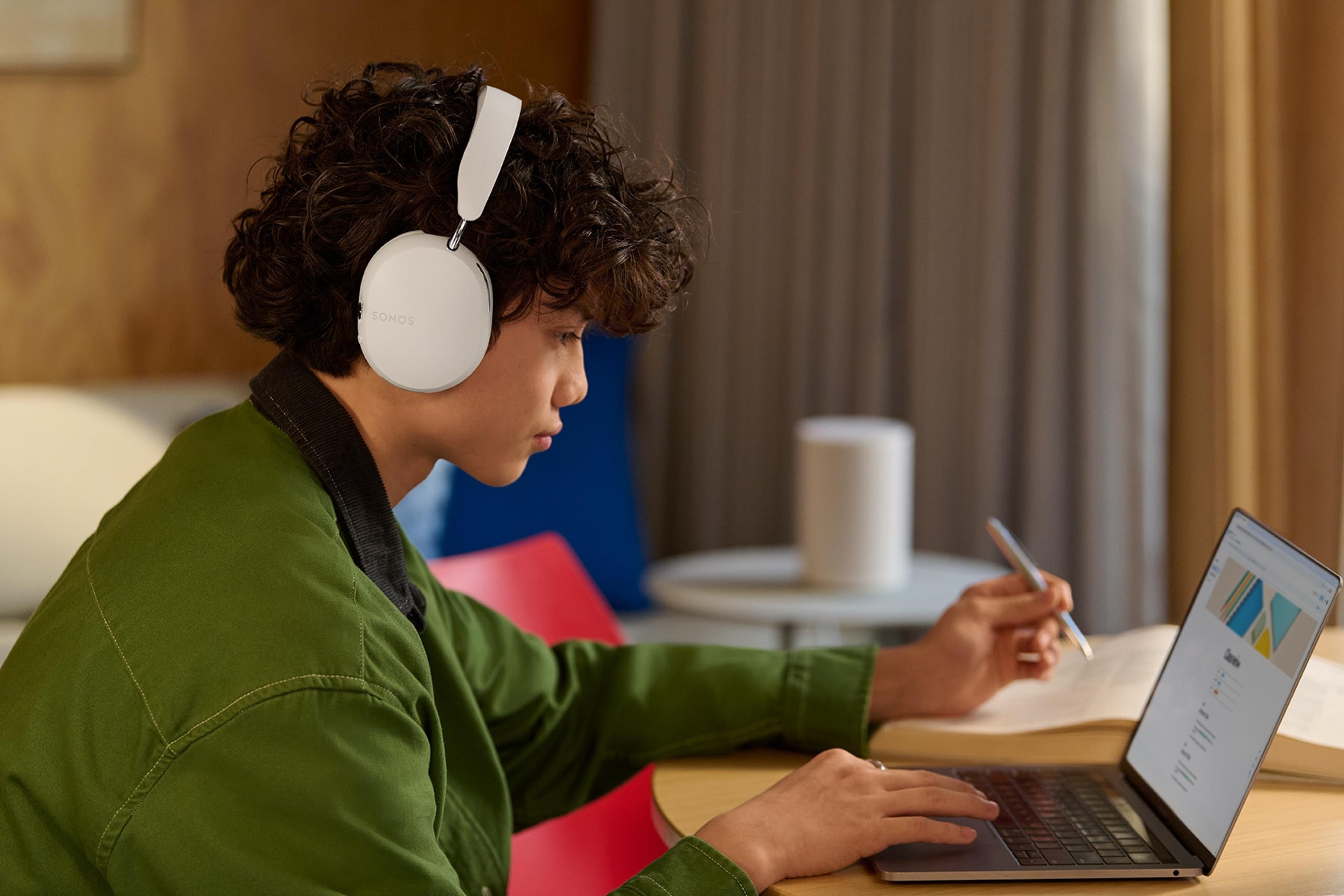 Student studying at laptop while listening to white Sonos Ace headphones
