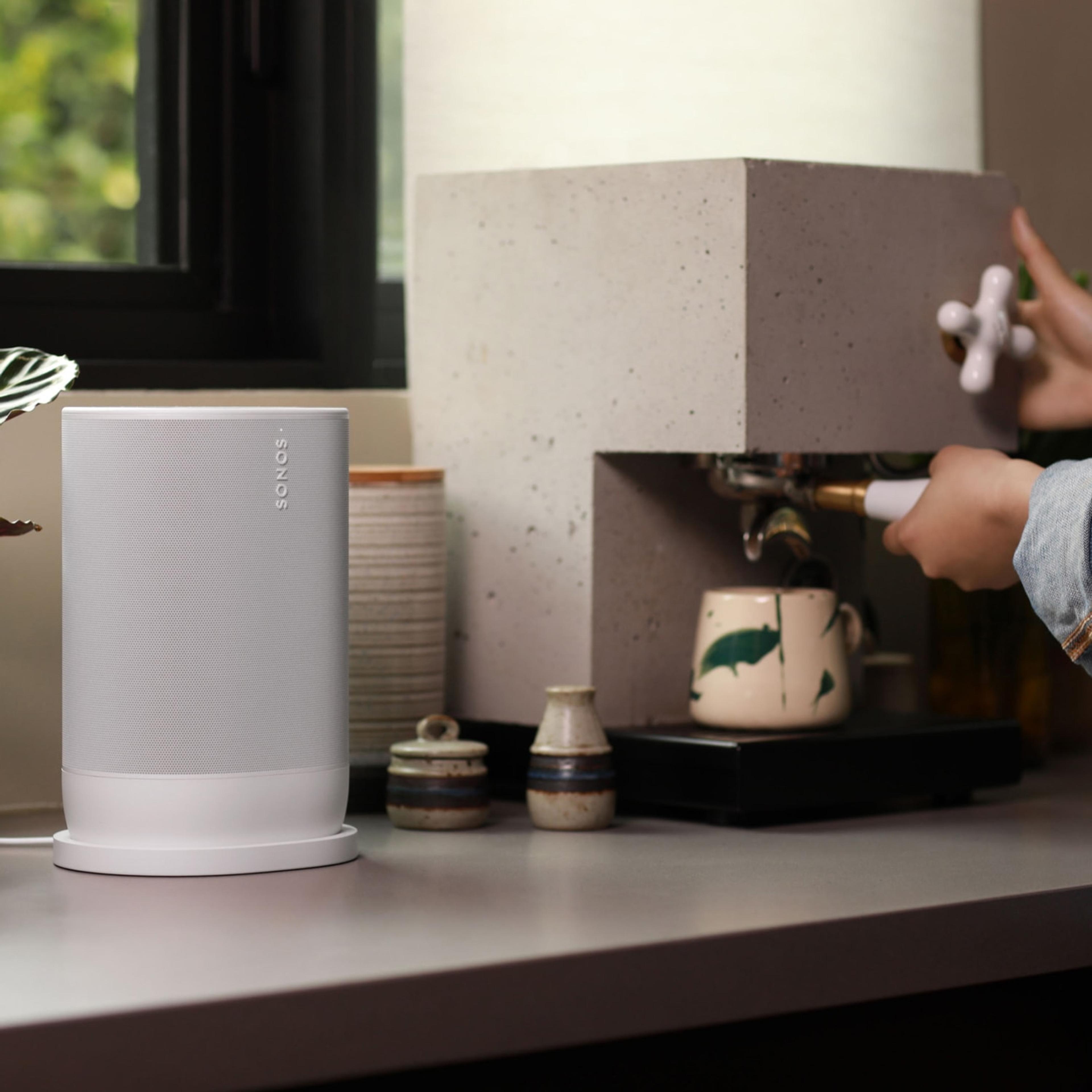A photo of a woman making espresso at the kitchen counter next to a white Sonos Move 2