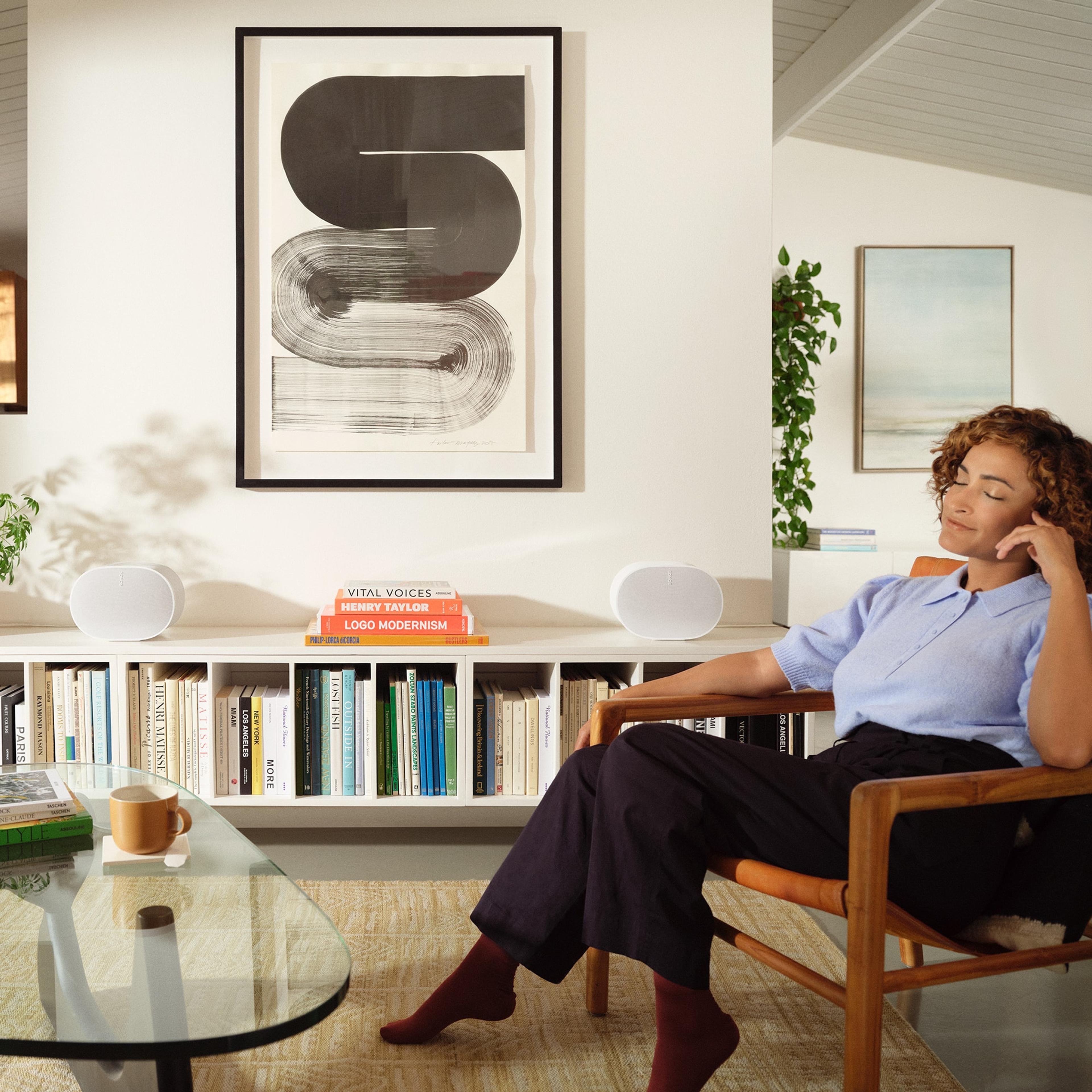 A woman seated in her living room listening to a pair of white Era 300 speakers